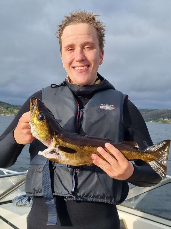 Sivert i våtdrakt holder opp en fisk i båten